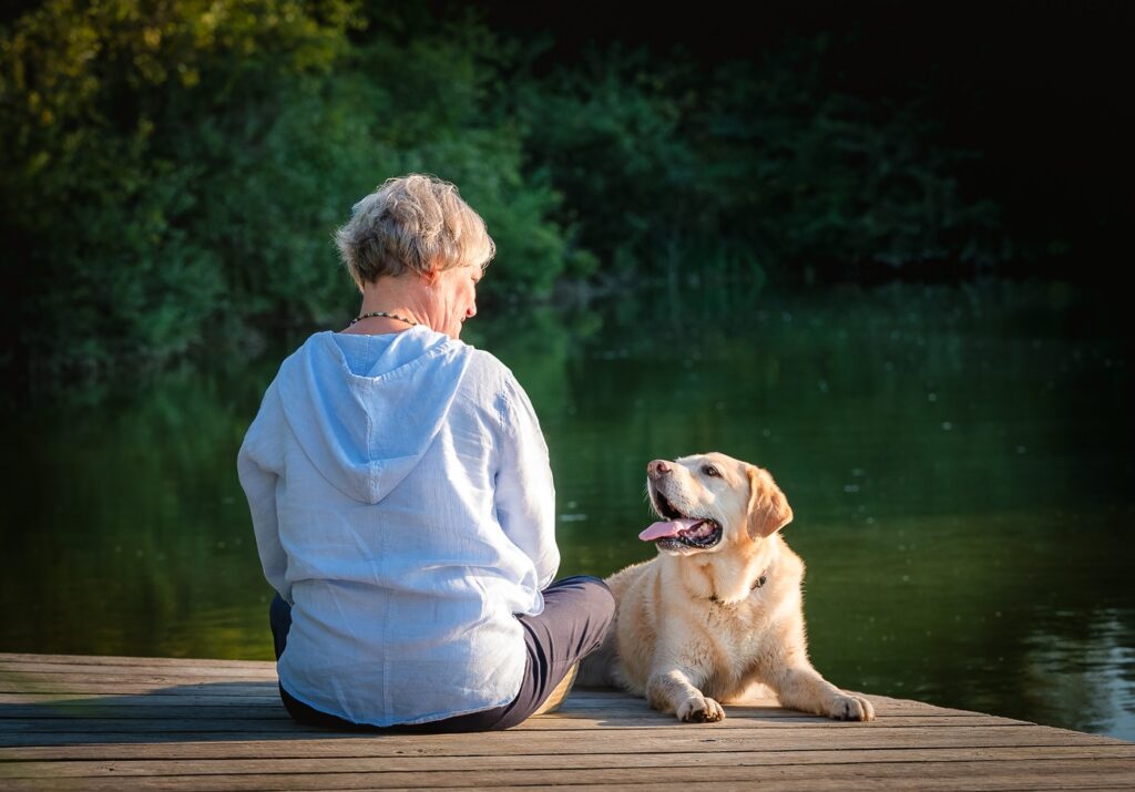 Woman sitting on a dock with her senior dog looking up at her during a senior dog photography session