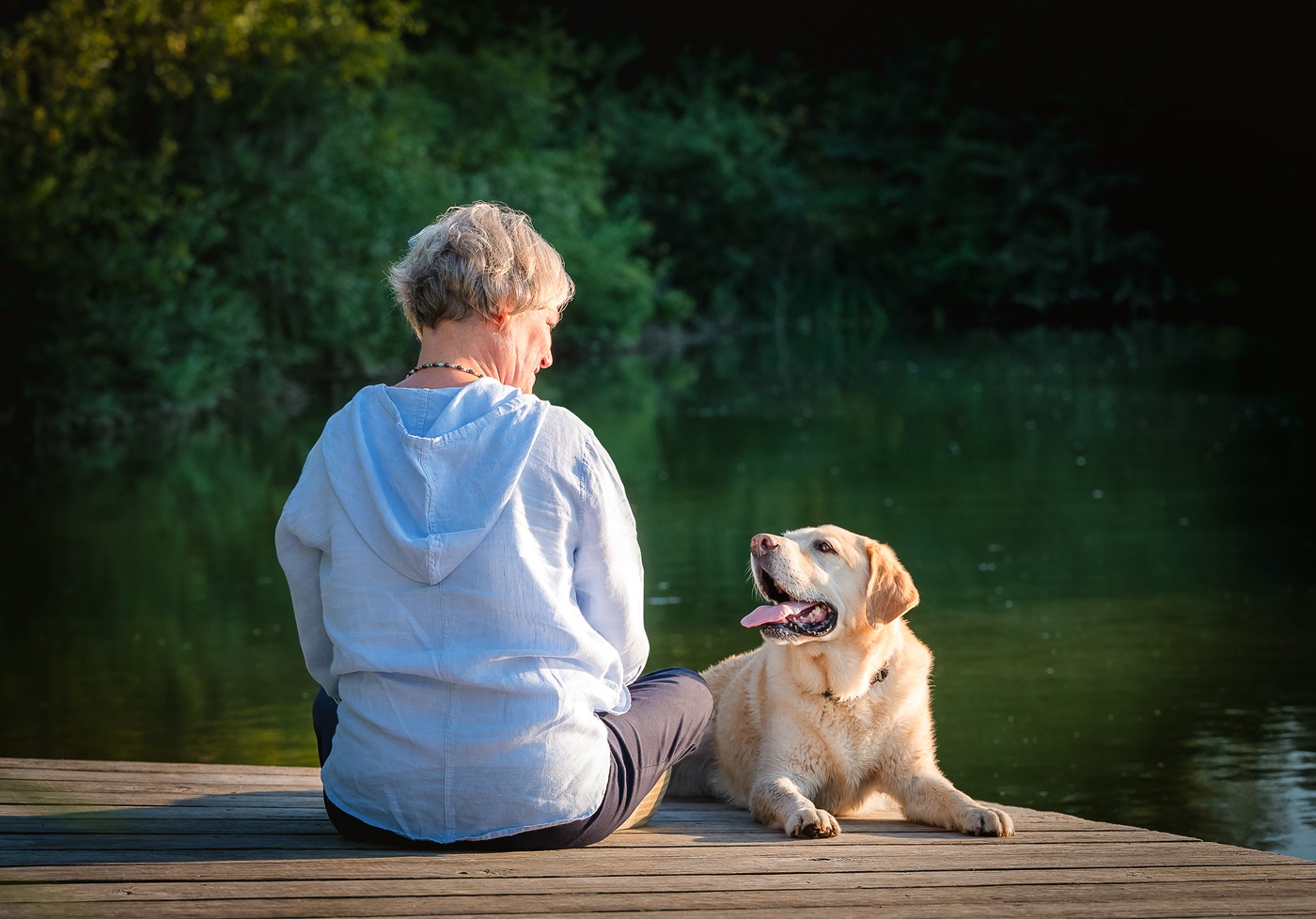 Woman sitting on a dock with her senior dog looking up at her